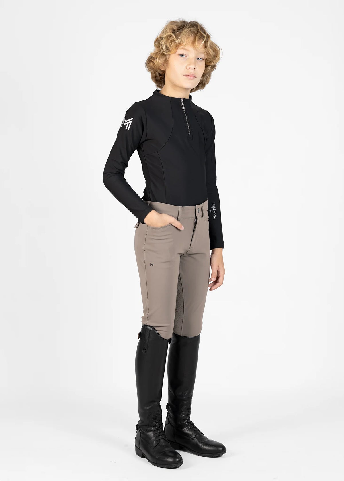 Person wearing a black equestrian shirt, beige riding pants, and black riding boots on a white background